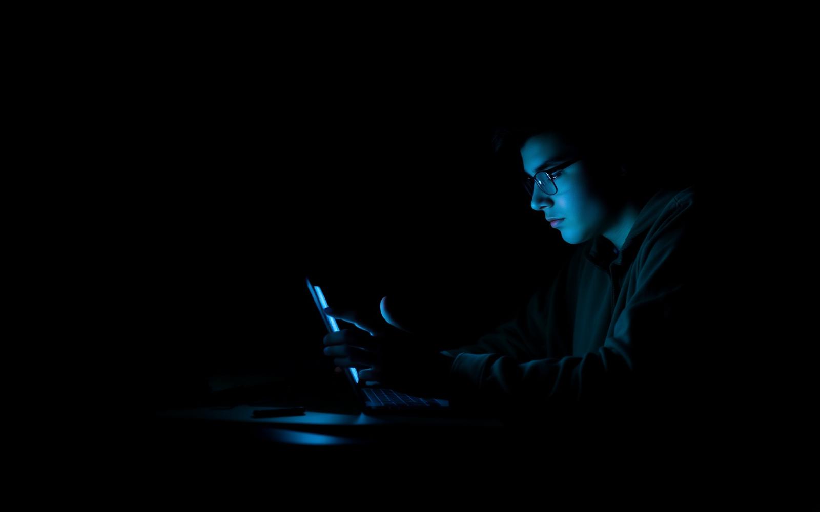 College student studying at a desk at night beside a glowing phone screen.